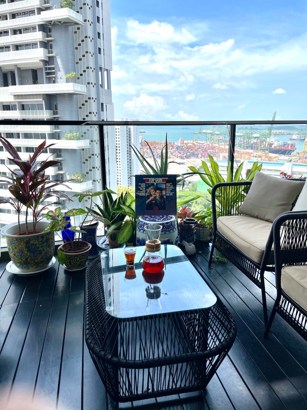 A pour-over carafe of coffee on a balcony table among potted plants, high above Singapore's container port